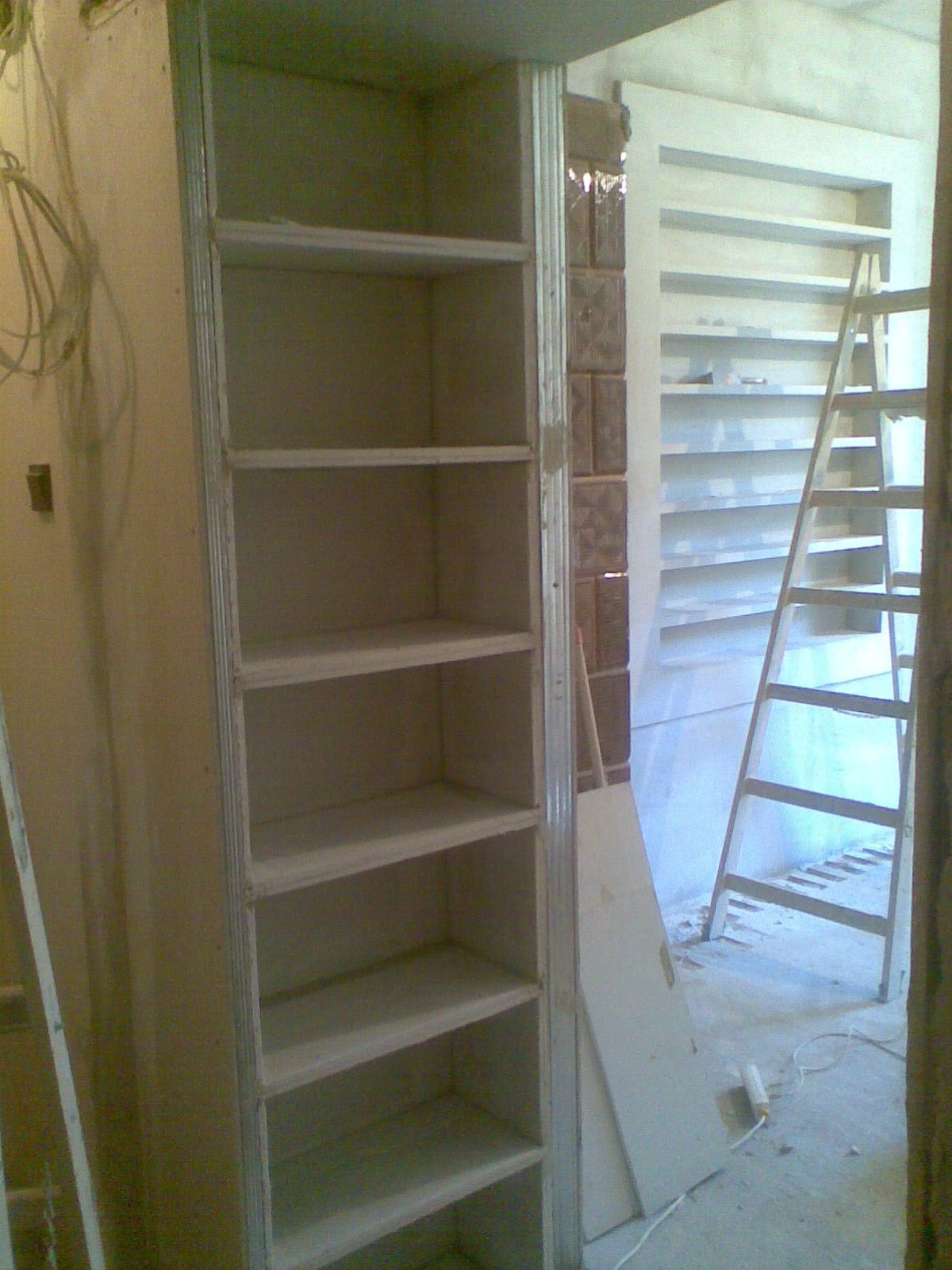 Montaż szkieletu szafy wnękowej z płyt kartonowo-gipsowych, widoczna drabina i fragment ściany z dekoracyjną cegłą.